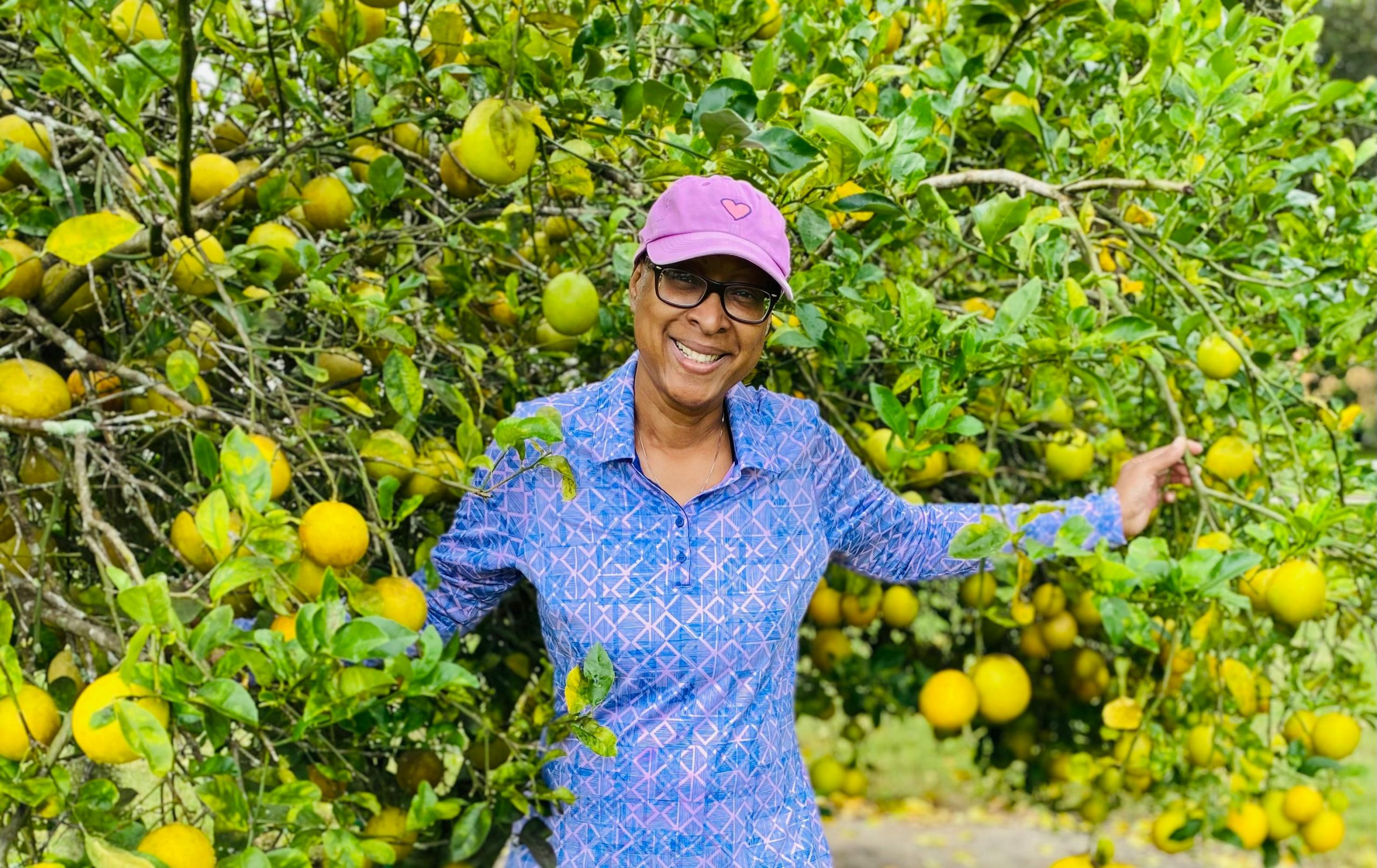 smiling woman wearing a pink cap standing in front of a lemon tree